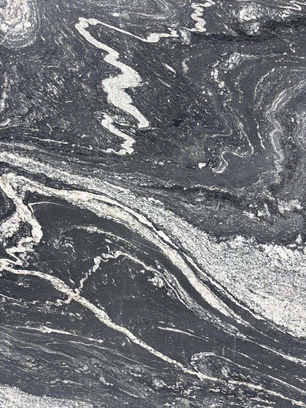 Black Storm granite detail, swirling grey and white quartz currents folding through a deep black ground