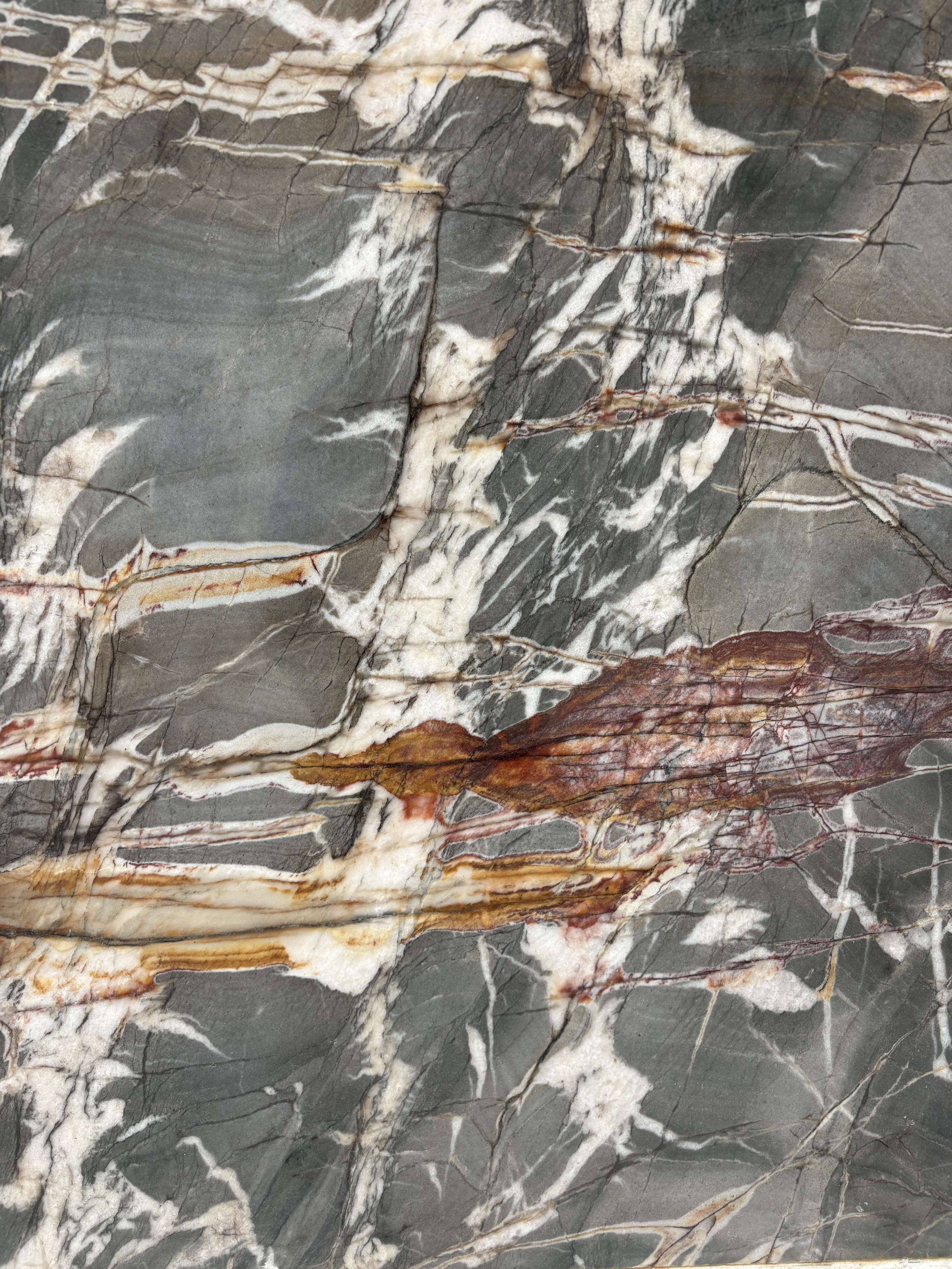 Venom quartzite detail, rust-red and amber seams running beneath white quartz veining on a slate ground