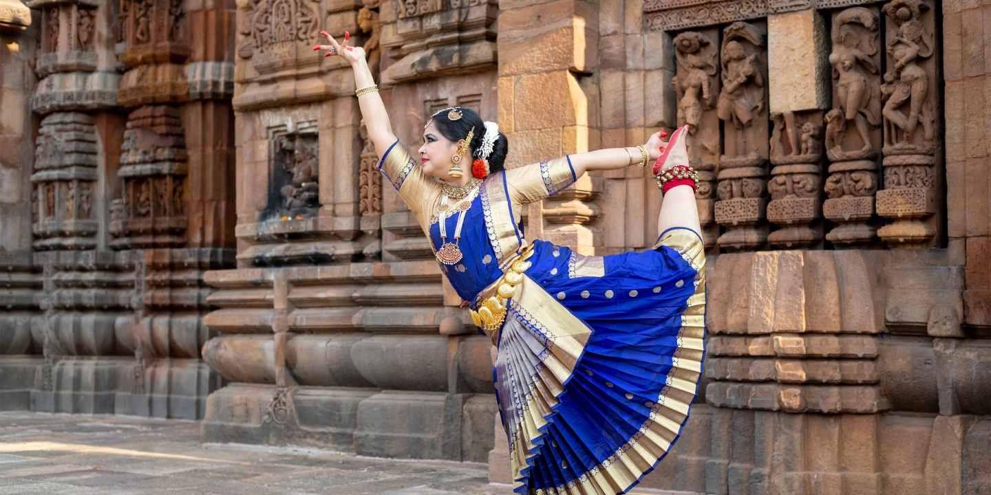 Bharatanatyam dancer in a blue costume performing before carved temple walls