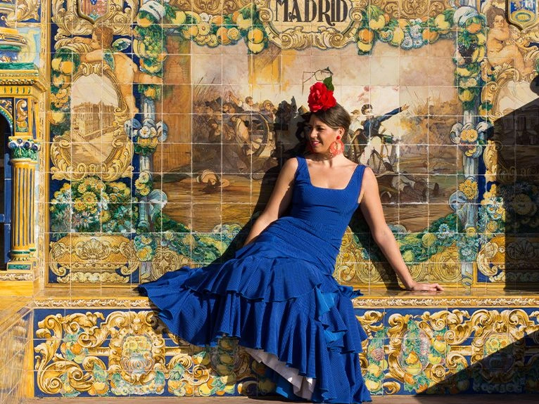 Woman in blue flamenco dress sitting against ornate Spanish tiles