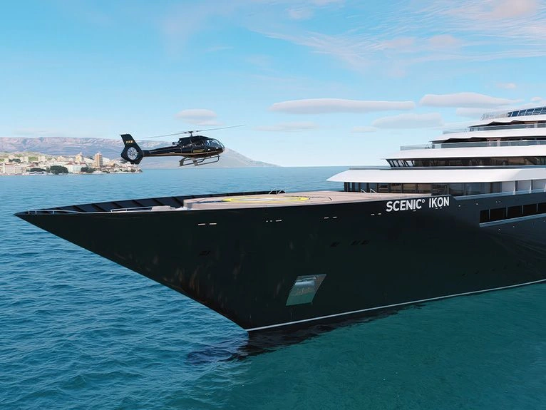 Scenic Ikon with helicopter approaching its bow helipad at sea