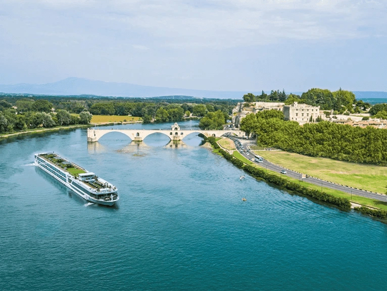 The Scenic Sapphire ship gliding on the waters of the Rhone River, next to a bridge and the captivating landscape of Avignon, France.  