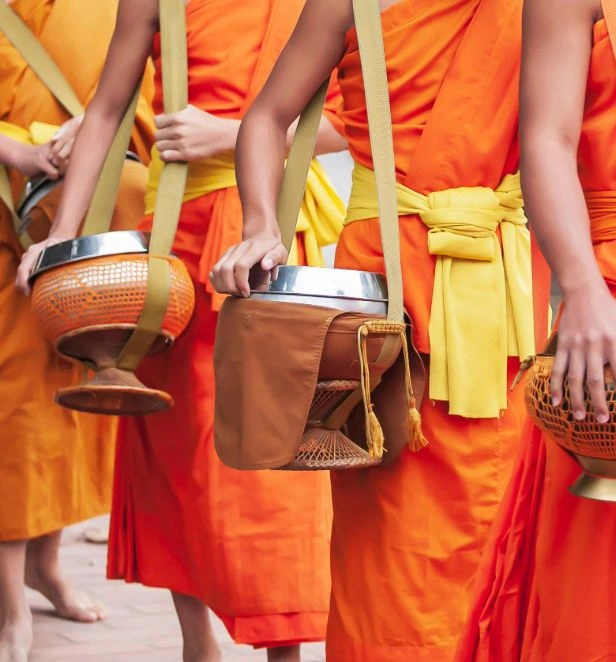 Several Buddhist monks in bright orange robes walk while carrying traditional alms bowls.