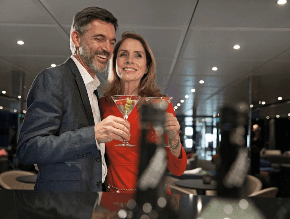 Smartly dressed man and woman smiling as they drink martini cocktails 