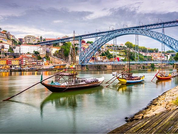 A view of Porto, Portugal, taken from under the Dom Luís bridge. Three small boats can be seen sailing on the Douro River.