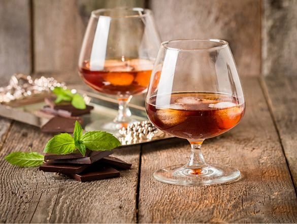 Glasses of delicious rum served with dark chocolates on a wooden board
