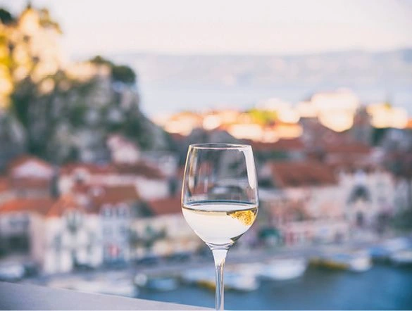 Crisp glass of white wine in front of a blurred backdrop of a coastal Mediterranean townic 