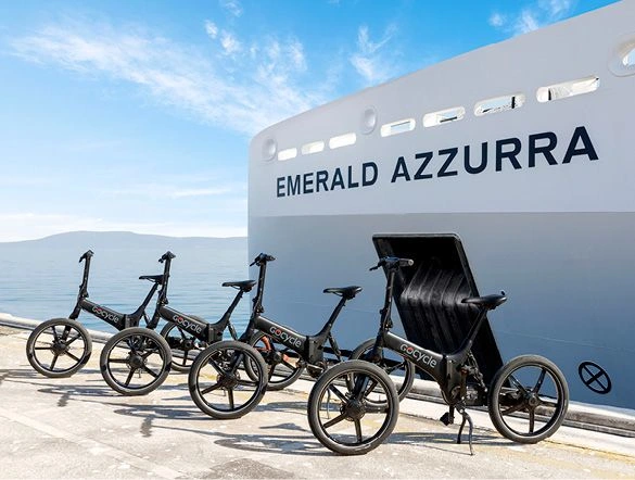 Four electric bikes lined up in front of a luxury yacht, with the blue, light cloudy sky above