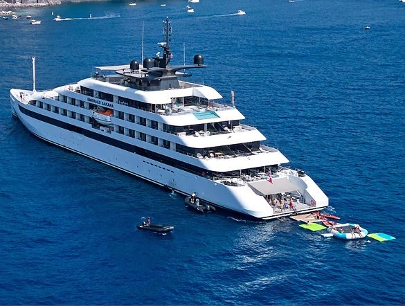 People paddleboarding in the sea next to a luxury yacht.