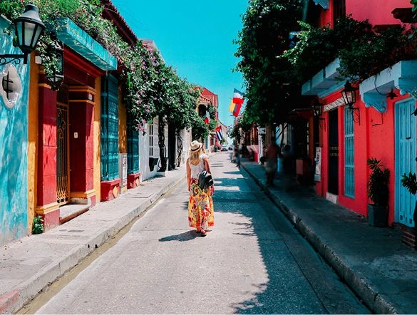  A woman wandering through a pretty street filled with colourful houses covered in greenery in Cartegena Columbia