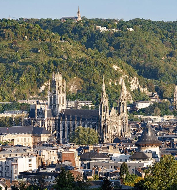 Panoramic view of Rouen’s skyline in Normandy, with the Gothic cathedral rising above the city and forested hills in the background.