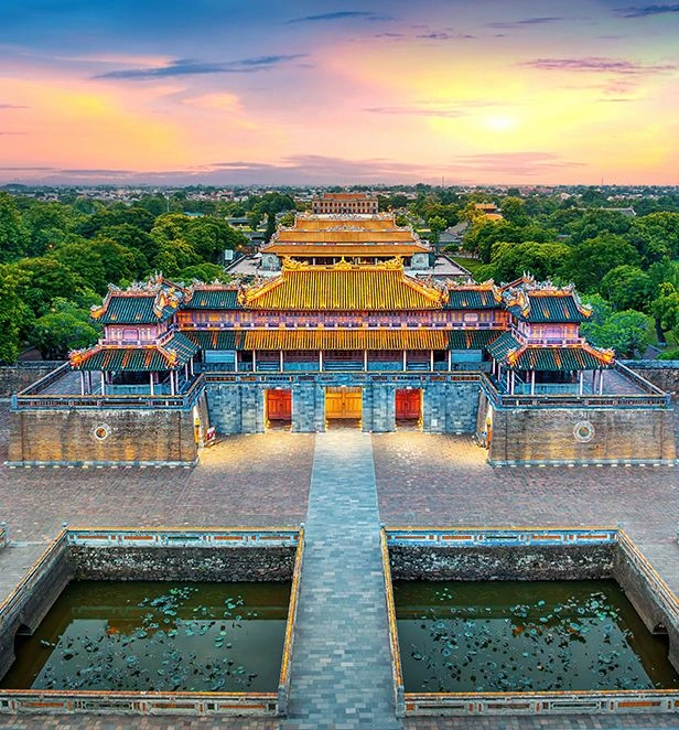 Meridian Gate at the Imperial Citadel in Hue, Vietnam, illuminated at sunset with its ornate roofs reflected in the surrounding moat.
