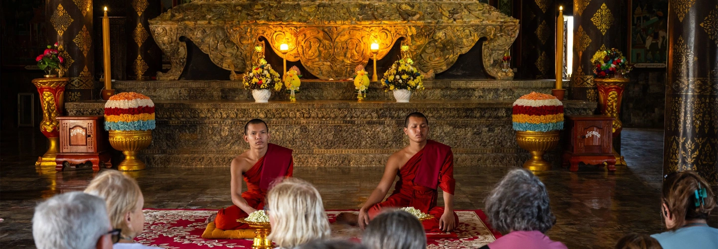 Buddhist monks seated before a temple altar as guests watch