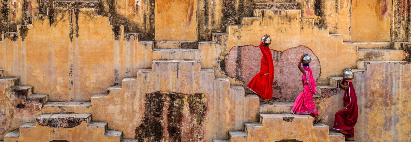 Three women carrying water pots climb the stepped walls of Panna Meena ka Kund in Jaipur