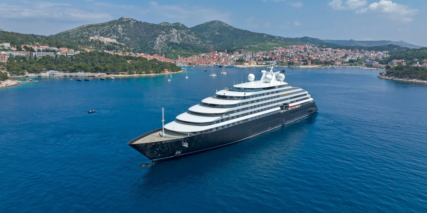 Scenic Eclipse Discovery Yacht anchored off a coastal town in calm blue water