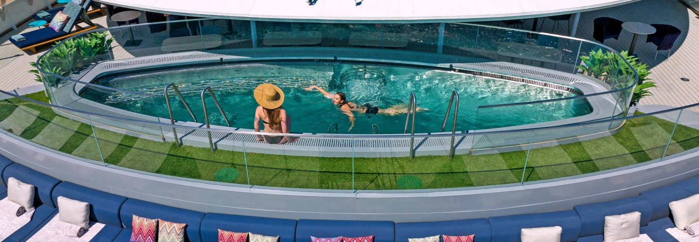 Two guests relaxing and swimming in a glass-edged pool on a Scenic Discovery Yacht deck