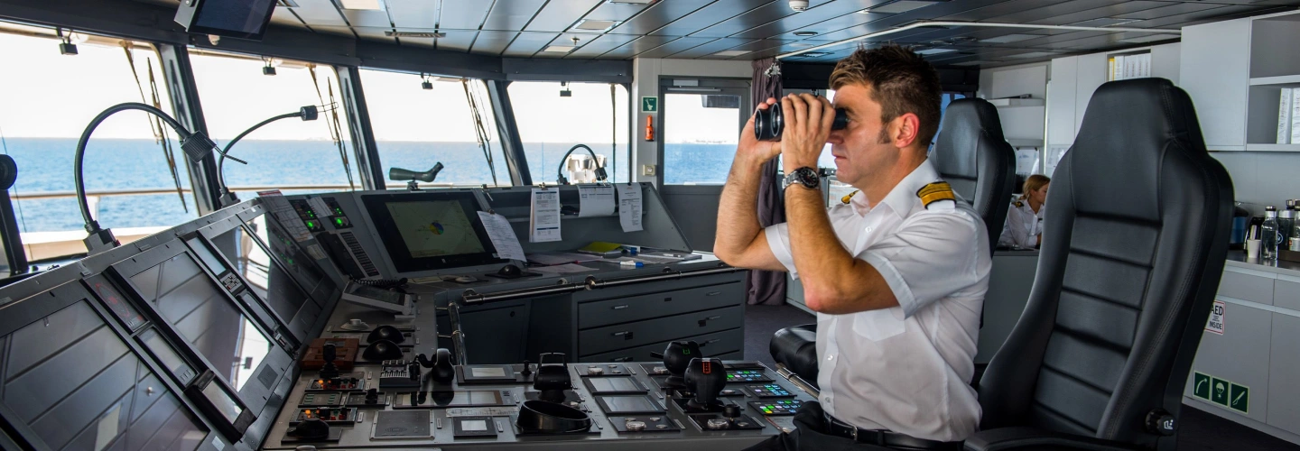 Ship officer on the bridge scanning the horizon with binoculars
