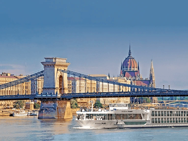 The Scenic Ruby Space-Ship sailing along the Danube River, with the Chain Bridge and the cityscape of Budapest in the background.