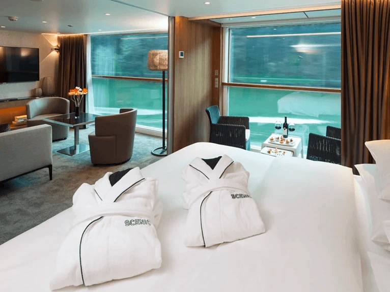 A Queen size bed adorned with plush white bathrobes in the Royal Balcony Suite, with floor-to-ceiling windows offering a view.