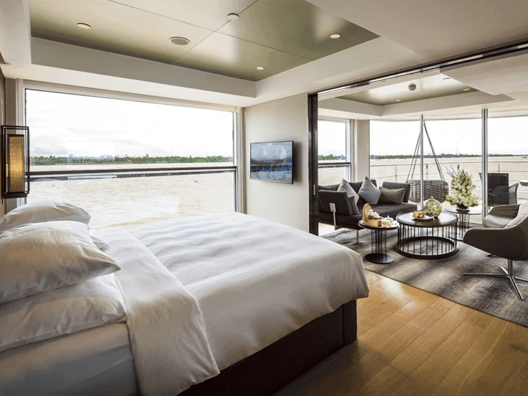 A Royal Panorama Suite on the Scenic Spirit ship, with a Queen bed and a separate lounge area and river views from the floor-to-ceiling windows.