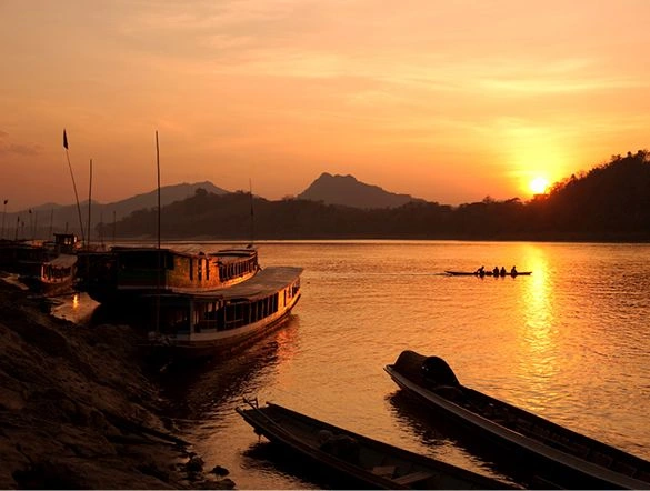 Bright orange sunset over the hills and reflecting on the water of the Mekong river with silhouettes of boats on the water