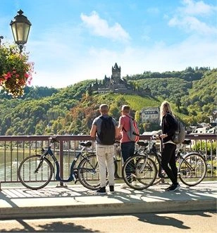 Three cyclists stopping to enjoy the views of Cochem Castle and the surrounding lands on a sunny day along the banks of the Rhine River