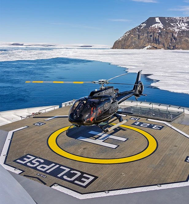Helicopter on cruise ship landing pad with water and snow in background