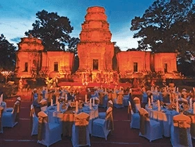 Tables set for dinner in front of an illuminated Angkor Wat temple 