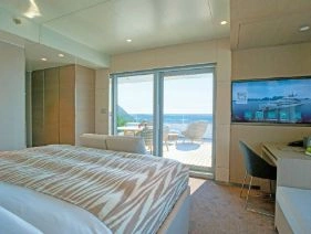 A large yacht suite with double bed and large balcony doors letting the bright sunlight in