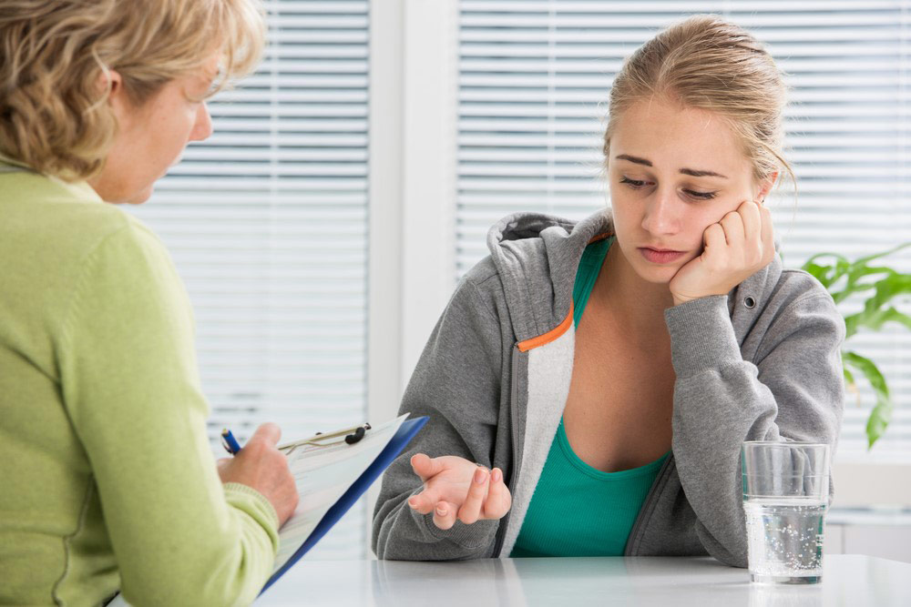 A counselor speaking with a young girl and taking notes at a table.