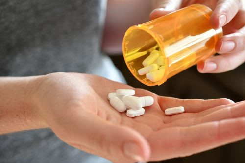 Female hands taking pills from an orange pill container