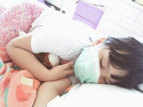 Little Girl With A Surgical Mask Sleeping Ill While Holding a Teddy Bear