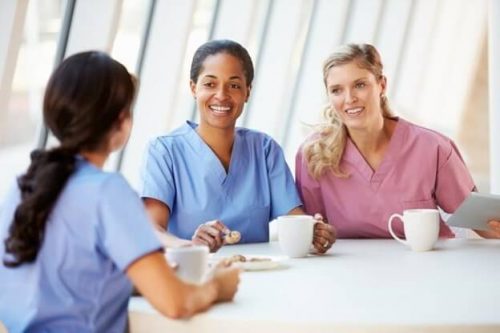 Smiling nurses drink coffee in a break room.
