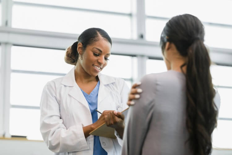 A smiling nurse writes down a patient’s information on a clipboard.