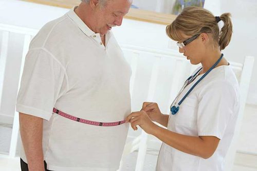 A female nurse measuring waist size of an elderly male patient