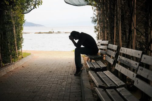 Silhouette of man sitting with head in hands on bench