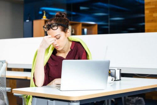 Red haired female with a green blanket around her shoulders holding her head from exhaustion 
