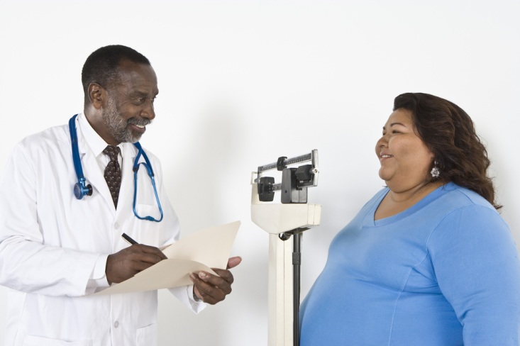 African American male doctor taking weight measurements of an overweight female patient