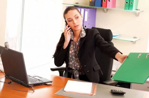 A nursing home administrator speaks on the phone while reviewing files.