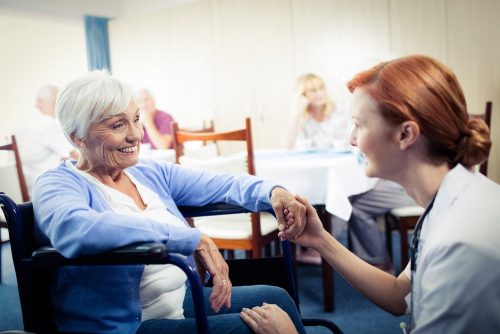 A female nurse talks to a woman in a wheelchair in a nursing home.