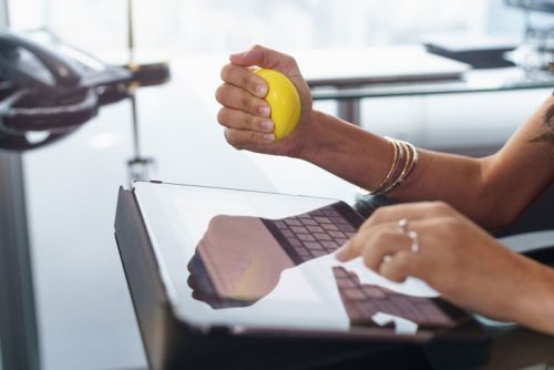 Female hands holding a yellow stress ball while typing at the keybord