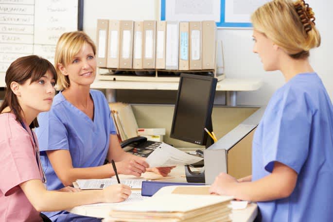 Three health care providers talk around the admitting desk.