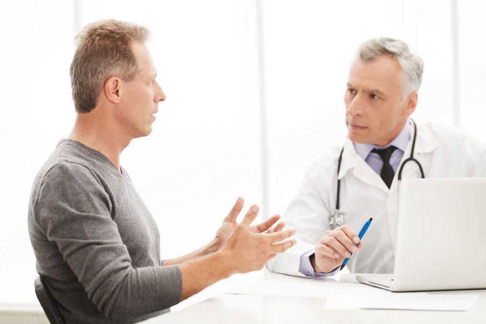 Middle aged male patient in a grey sweater talking to a male doctor with grey hair