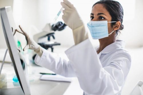 Epidemiologist looks at a testing vial in a lab. 