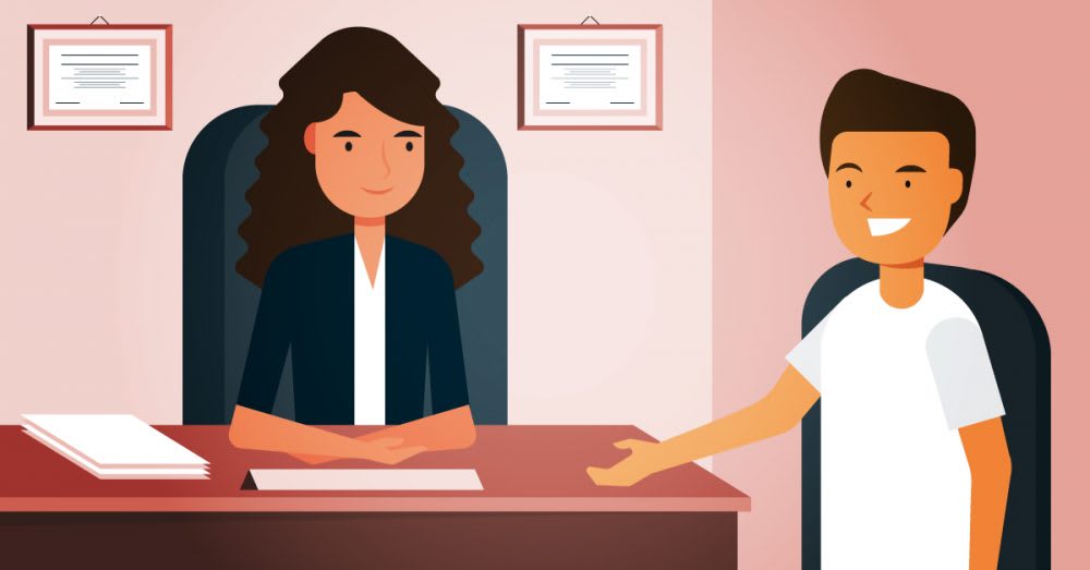 A college counselor sitting behind a desk with a student seated beside the desk.