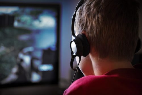 Boy in a red shirt sitting in front of a computer screen with a head set on 