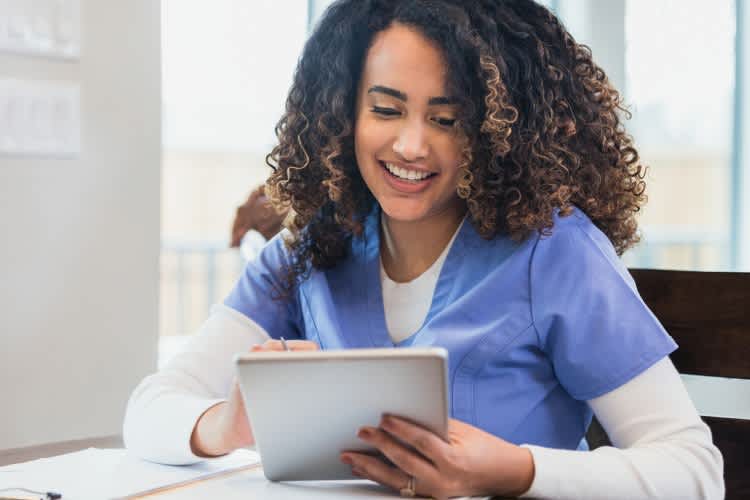A young nurse practitioner is responding to a comment from one of her social media followers using a digital tablet.
