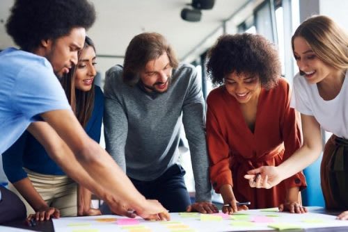 A diverse project team gathers around a project calendar filled with sticky notes.