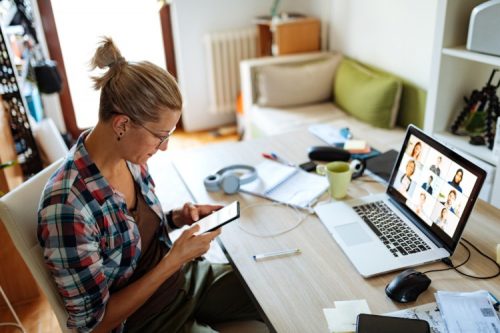 A worker in a home office meets with a virtual team using conferencing software on a laptop.