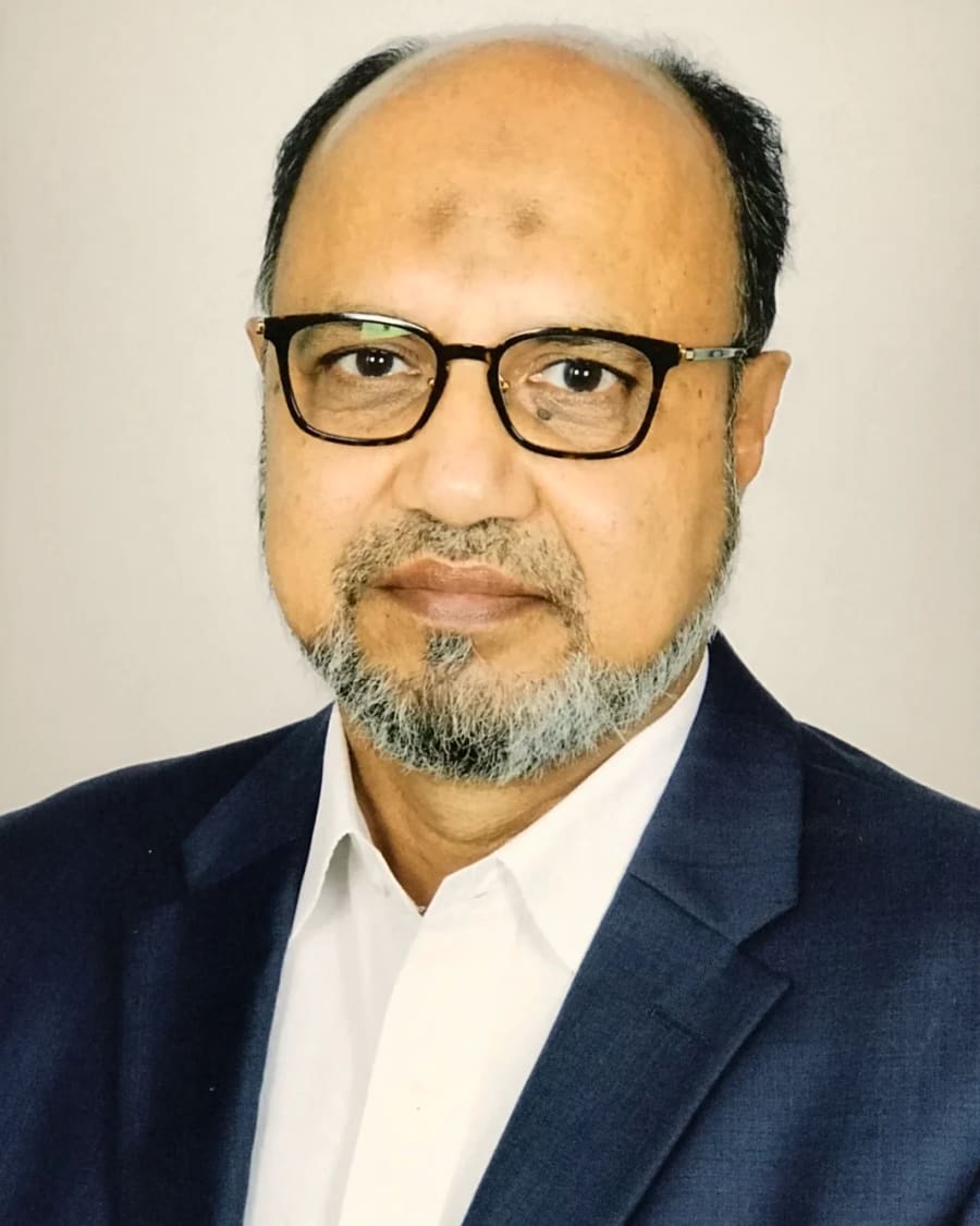 Portrait of the author in a green panjabi, seated beside a bookshelf